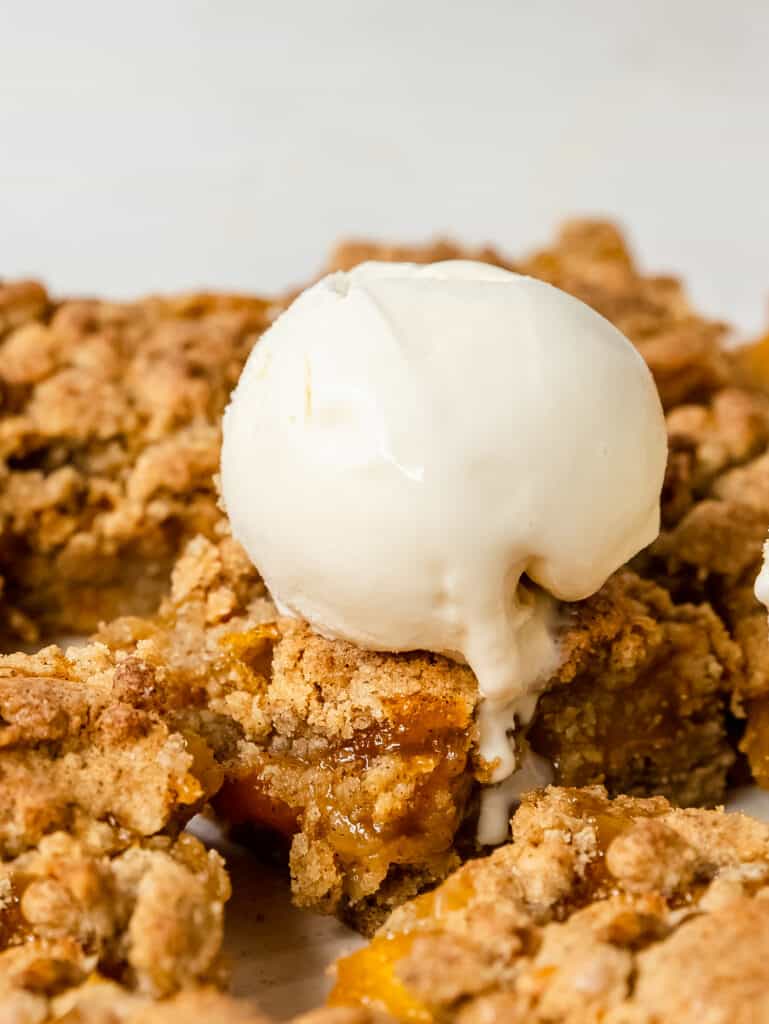 close up shot of peach crumble bars  topped with ice cream