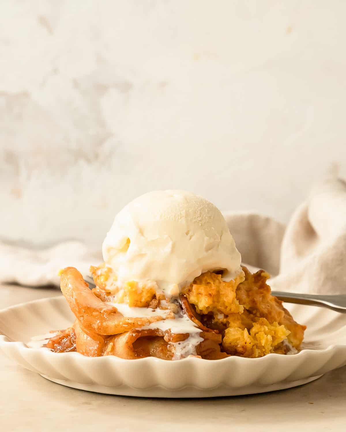 Apple Cobbler from Cake Mix on a plate with a scoop of vanilla ice cream melting on top. 