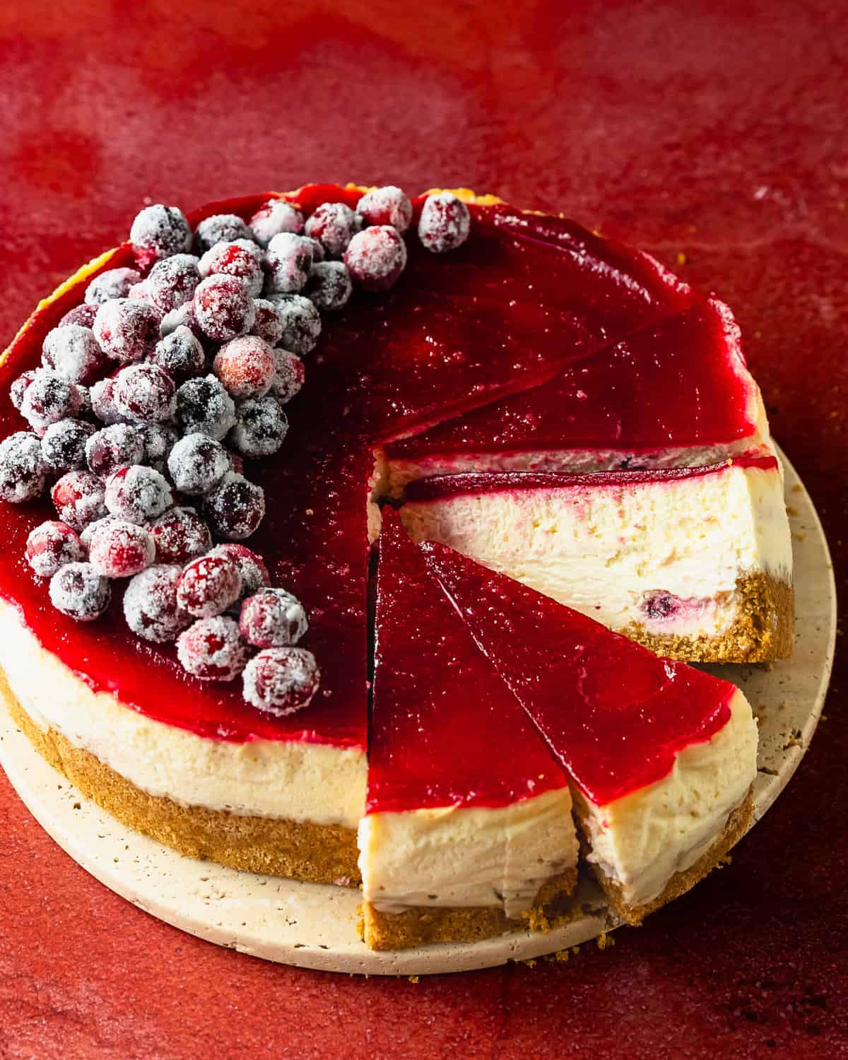 Cranberry cheesecake is a rich and creamy cranberry swirled cheesecake with a classic orange infused graham cracker crust. This decadent cheesecake with cranberries is topped with a beautiful ruby hued cranberry glaze and candied cranberries.  Make this cranberry topped cheesecake the next time you need a simple, stunning and celebratory dessert. 