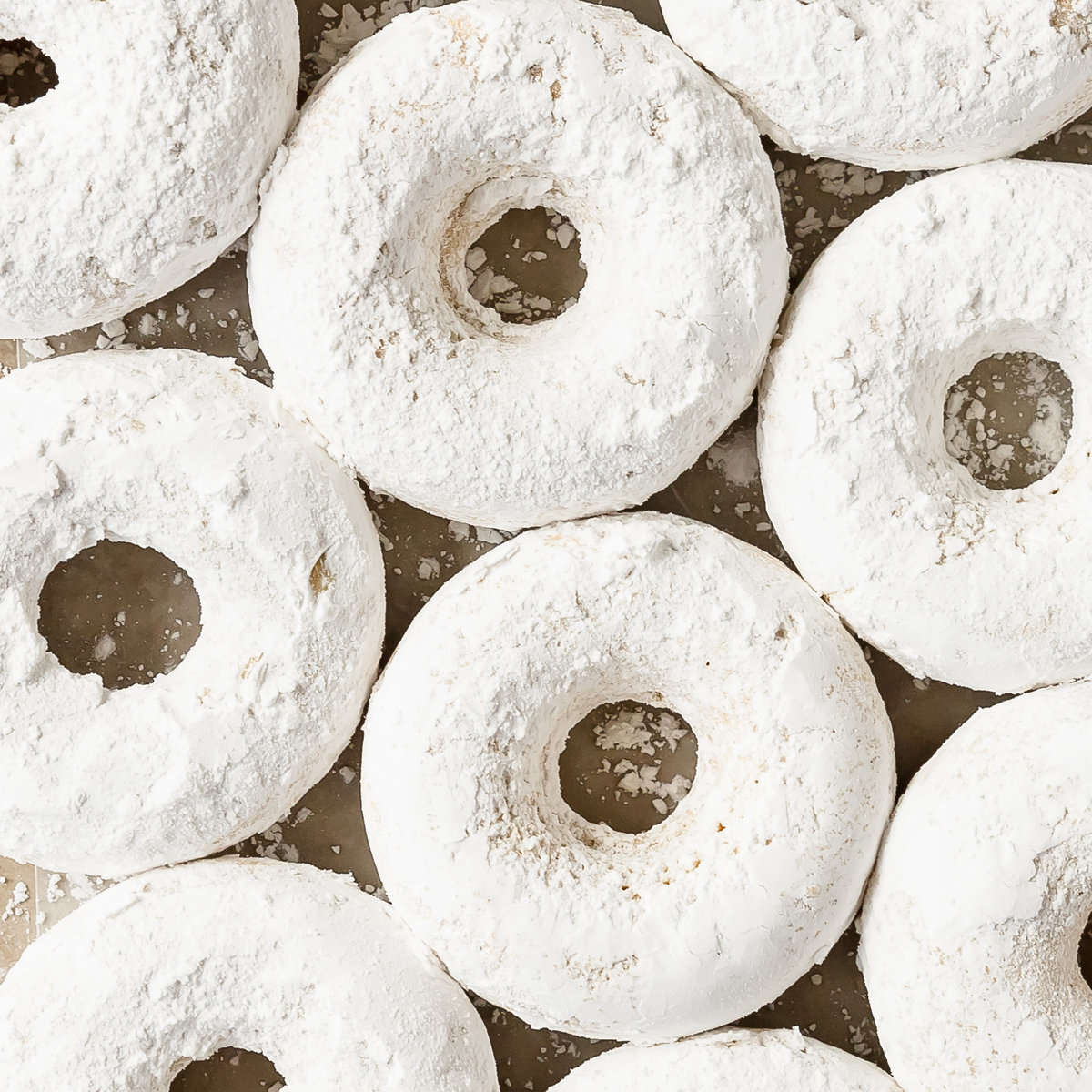 Powdered sugar donuts are soft, moist and fluffy, light;y spiced baked donuts coated in powdered sugar. These cake-style powdered donuts are quick and easy to make using two bowls, a whisk and a donut pan. If you can make muffins, you can make these cozy powder sugar donuts. 