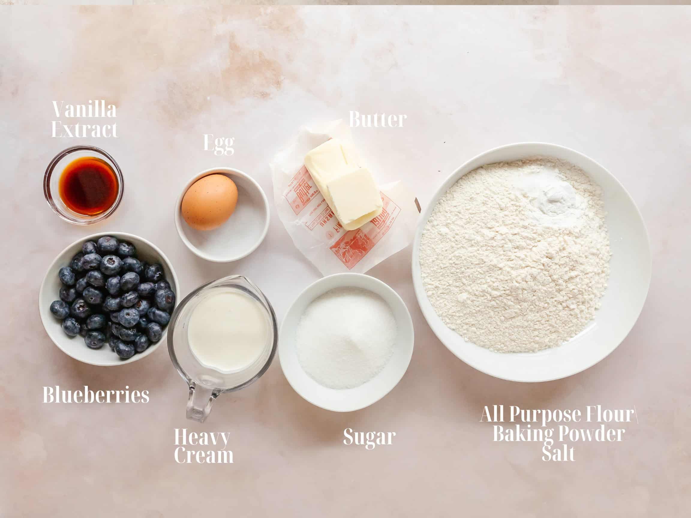 Blueberry scone ingredients: Flour, baking powder, salt, butter, sugar, vanilla extract, heavy cream, an egg and blueberries.