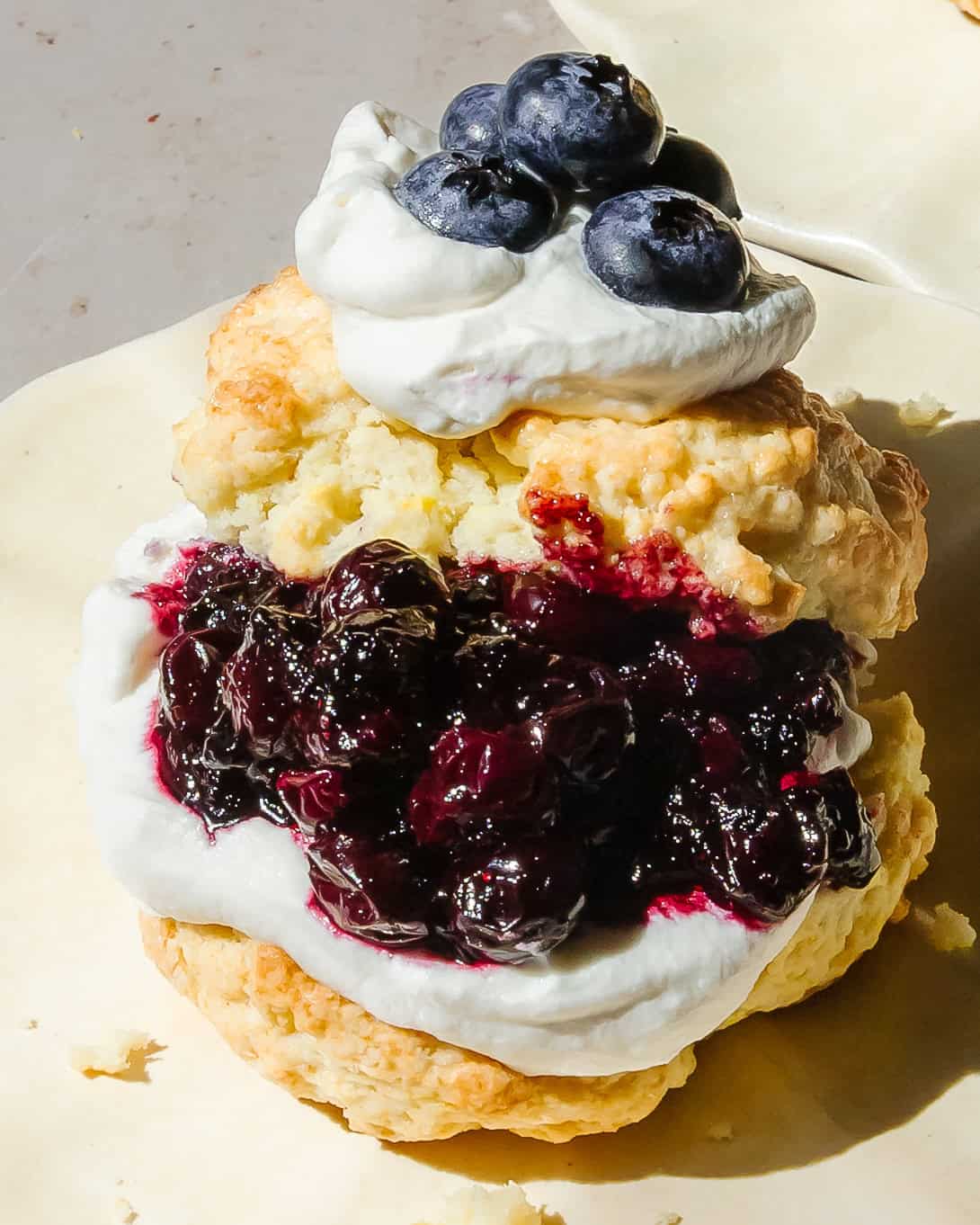 Homemade blueberry shortcake with buttery biscuit layers, fresh blueberry jam, and whipped cream dripping down the sides.