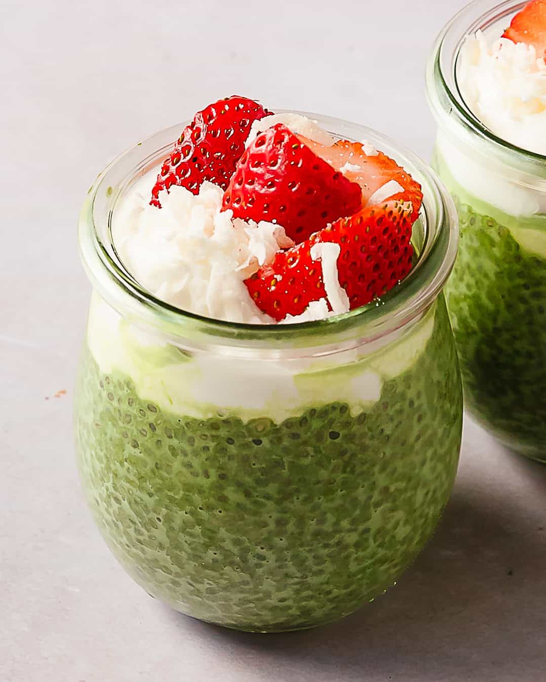 Matcha chia pudding in a jar topped with strawberries and coconut flakes.
