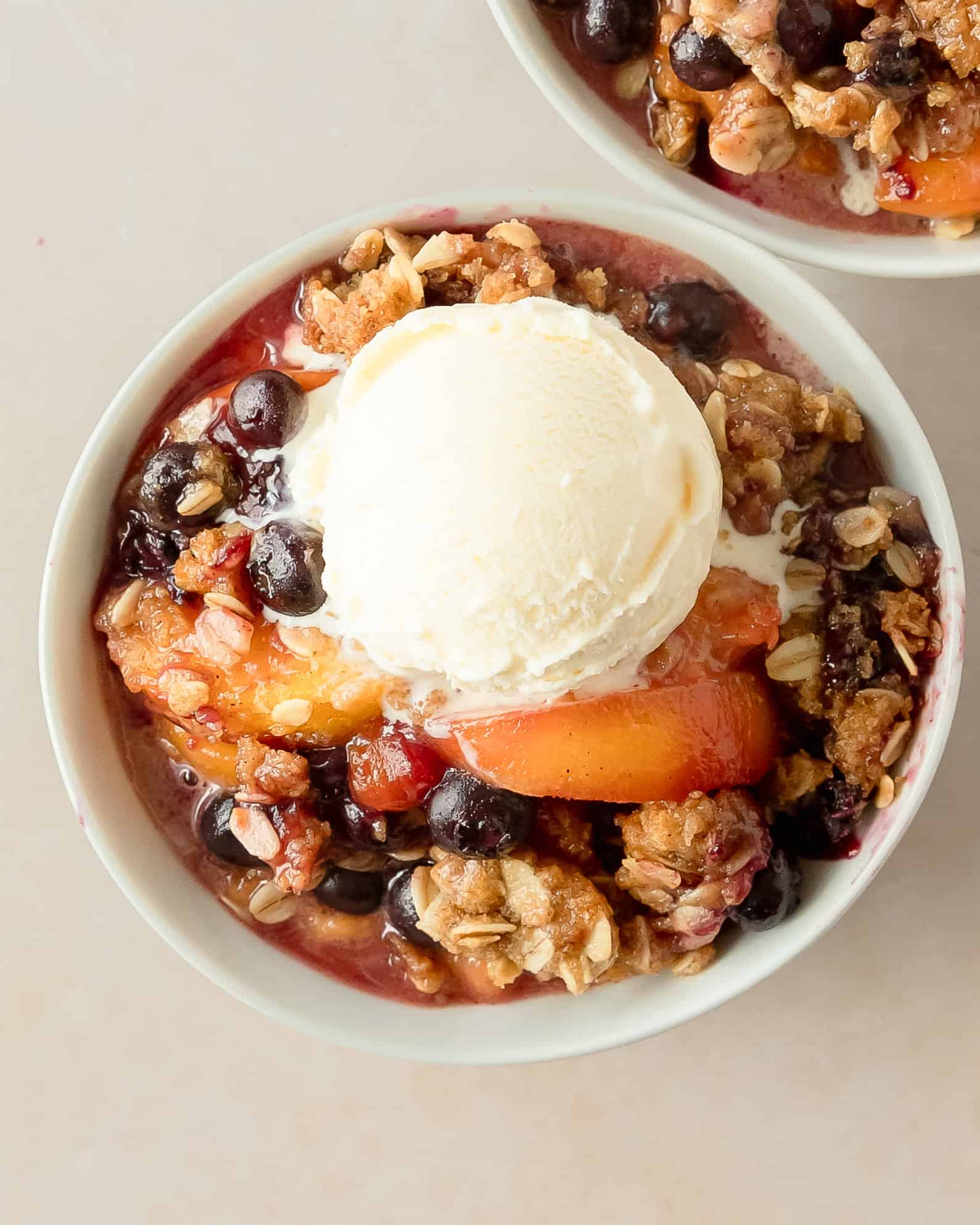 Homemade peach blueberry crisp topped with vanilla ice cream.