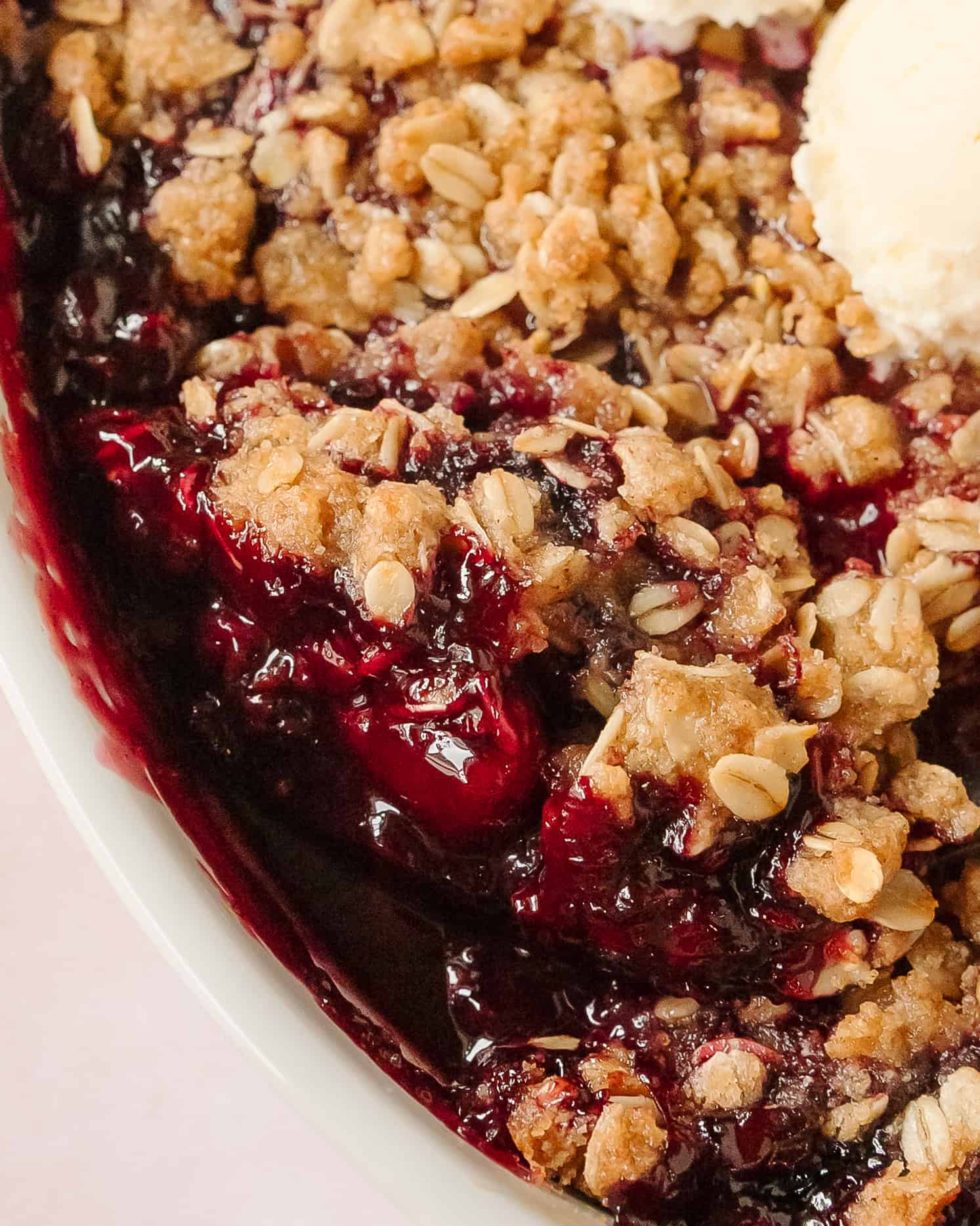 Spoonful of warm berry crisp showing layers of fruit filling and crumble.