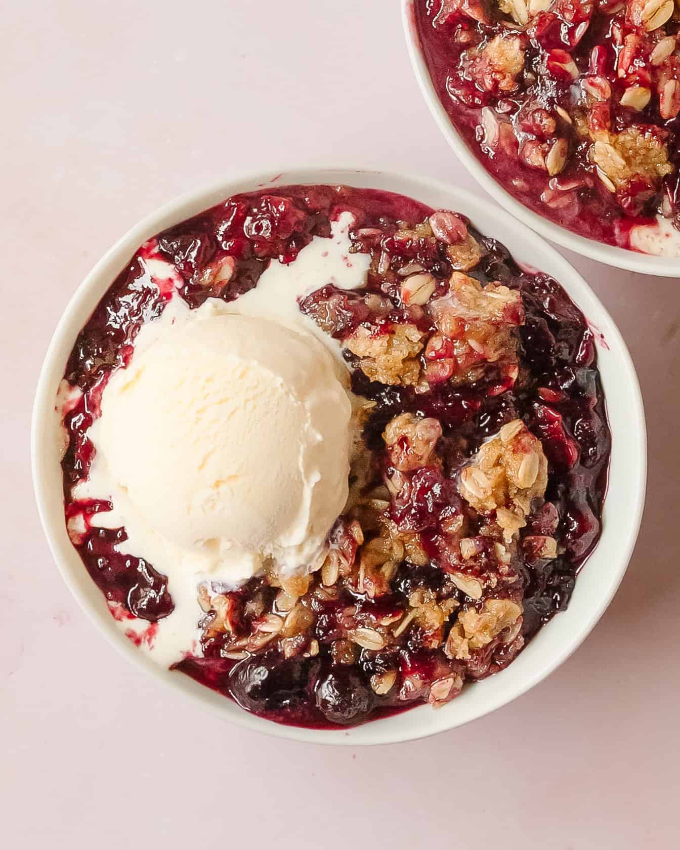 Berry crisp topped with vanilla ice cream melting into warm fruit filling.