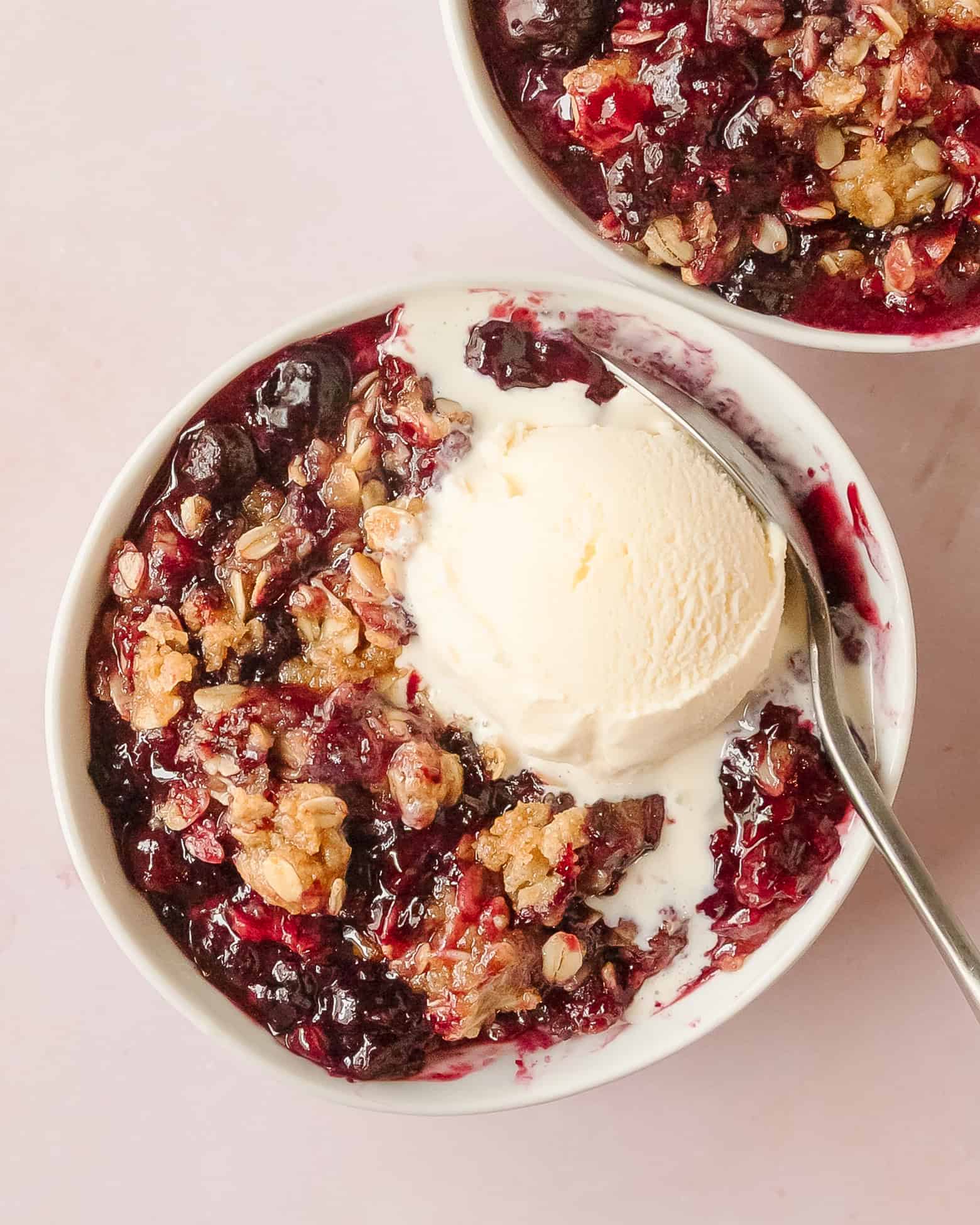 Scoop of berry crisp served in a bowl with melting vanilla ice cream.