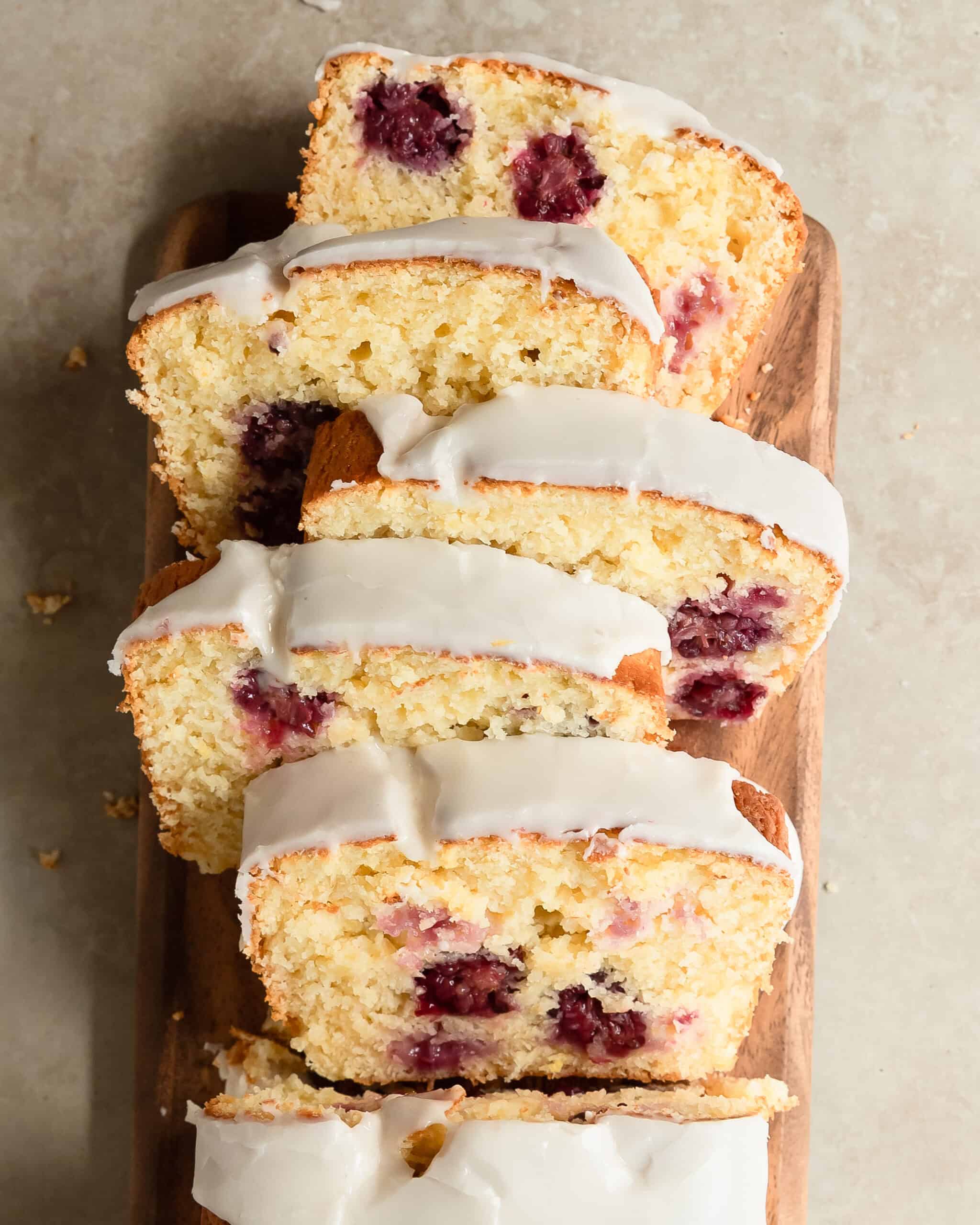 Glazed lemon blackberry loaf sliced on a serving platter, featuring fresh blackberries baked throughout.