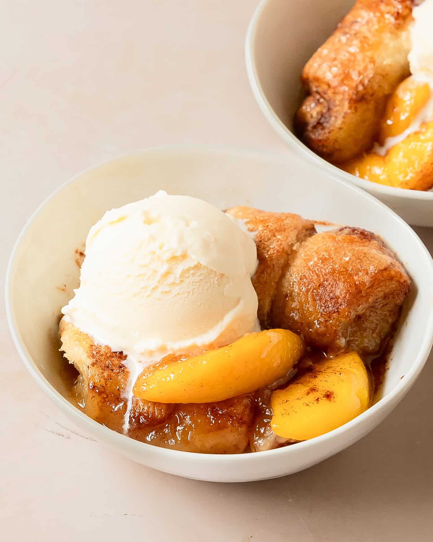 Homemade peach dumplings made with flaky pastry, fresh peaches, topped with ice cream.