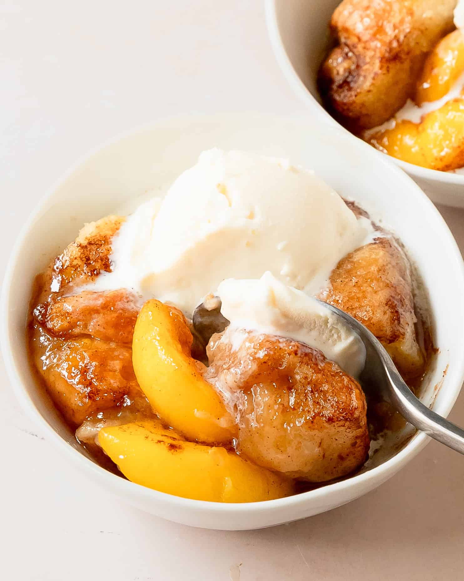 Easy baked peach dumplings made with fresh seasonal peaches, topped with vanilla ice cream.