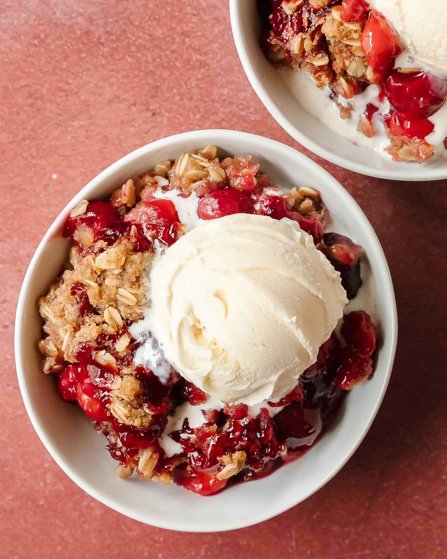 Homemade cherry crisp with juicy cherries and a golden buttery oat crumble topping and melting vanilla ice cream.