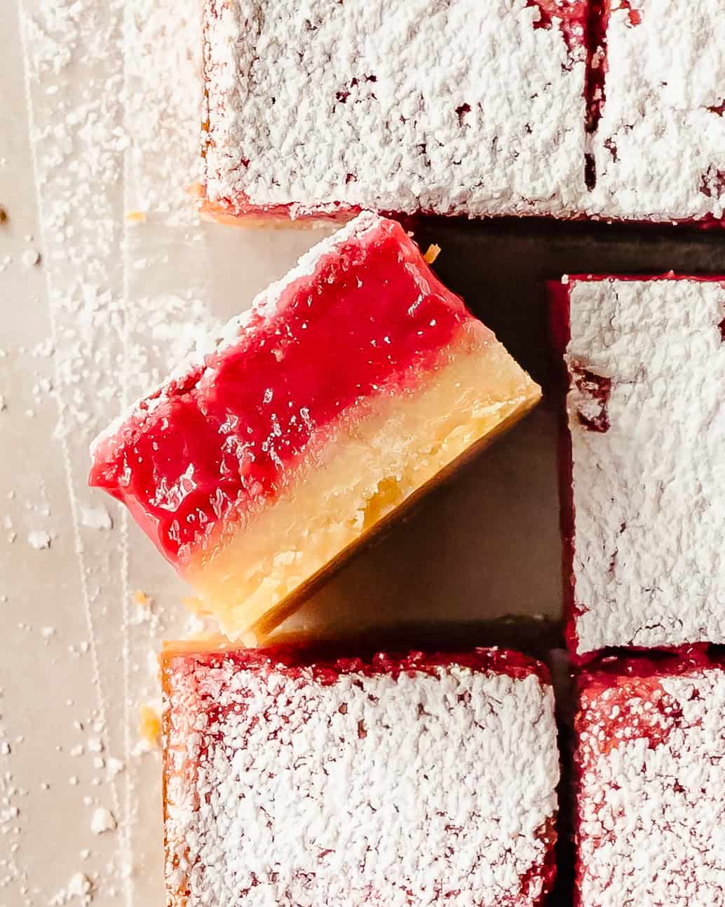 Close-up of a raspberry lemon bar showing the creamy lemon raspberry filling and buttery shortbread crust.