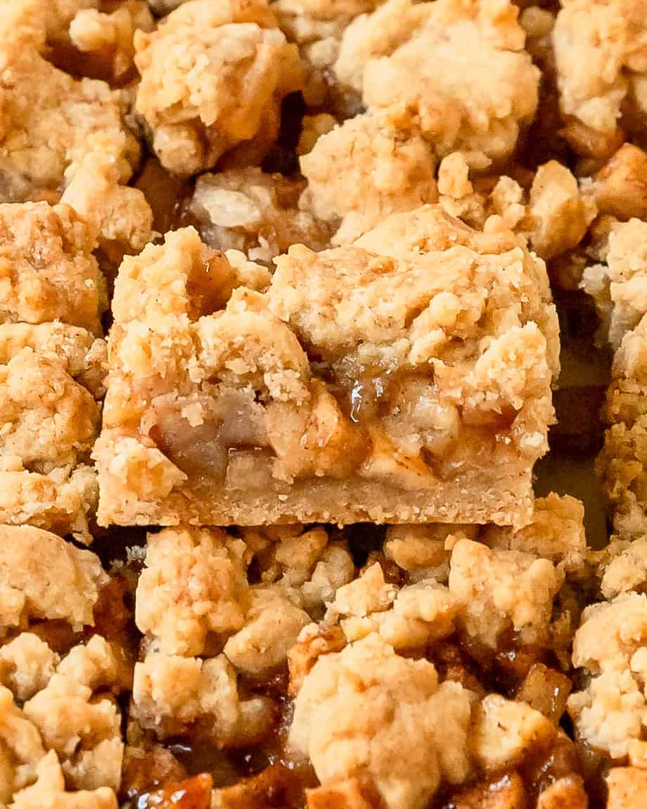 Close up slice of apple pie bar with layers of buttery crust, apples, and crumb topping.