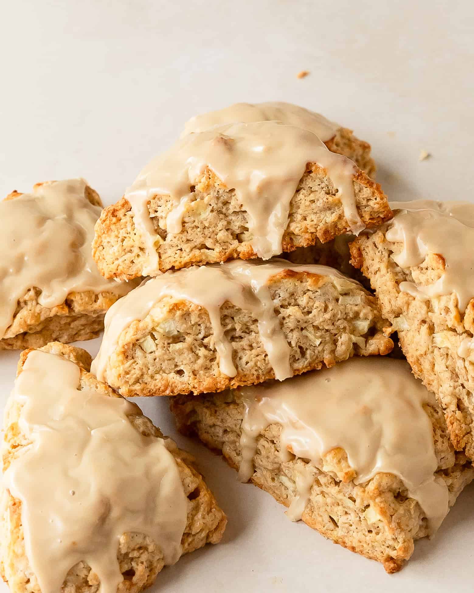 Freshly baked apple scones with visible pieces of apple and tall flaky layers topped with a maple glaze.