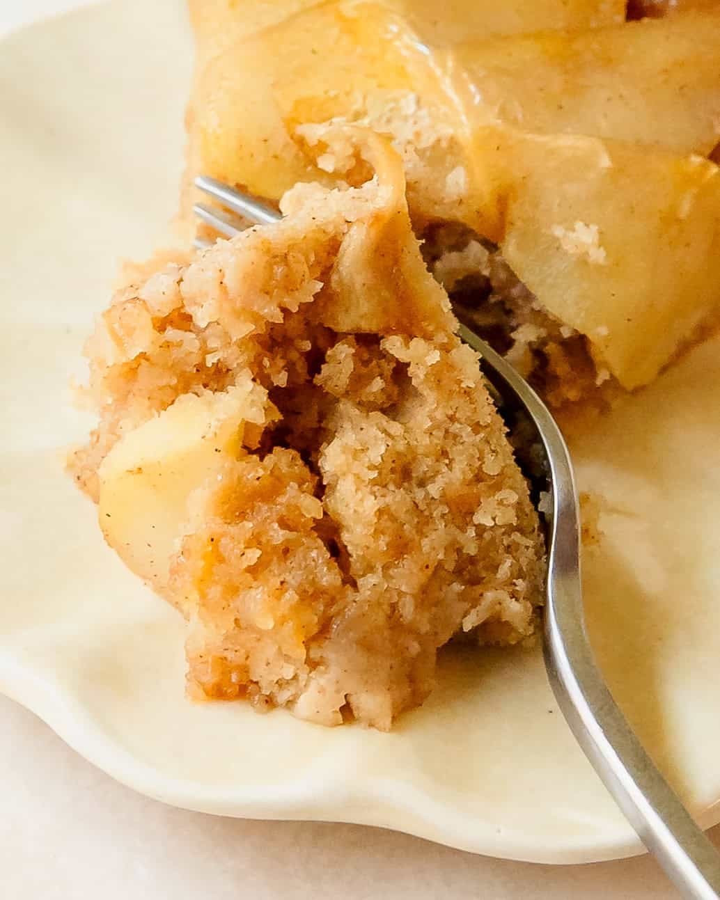 Slice of warm apple cake topped with caramelized cinnamon apples with a fork taking a piece.