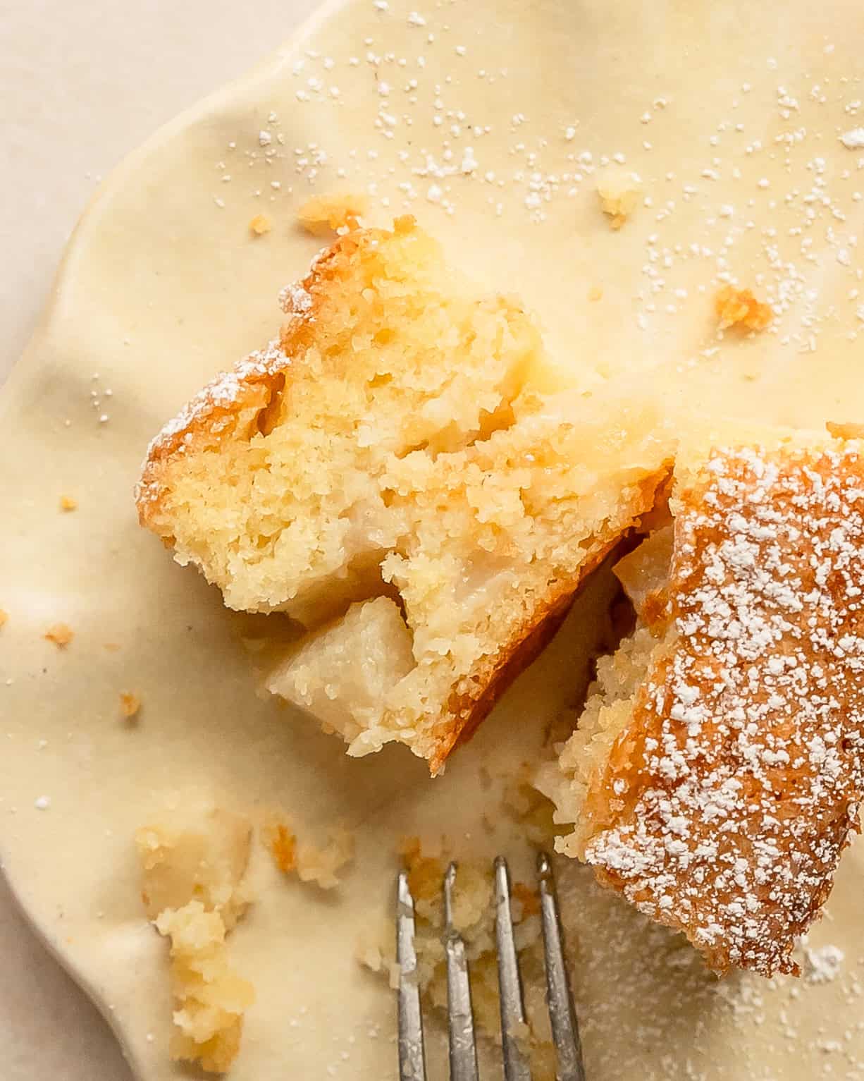 French pear cake showing pieces of baked pear throughout, dusted with powdered sugar.