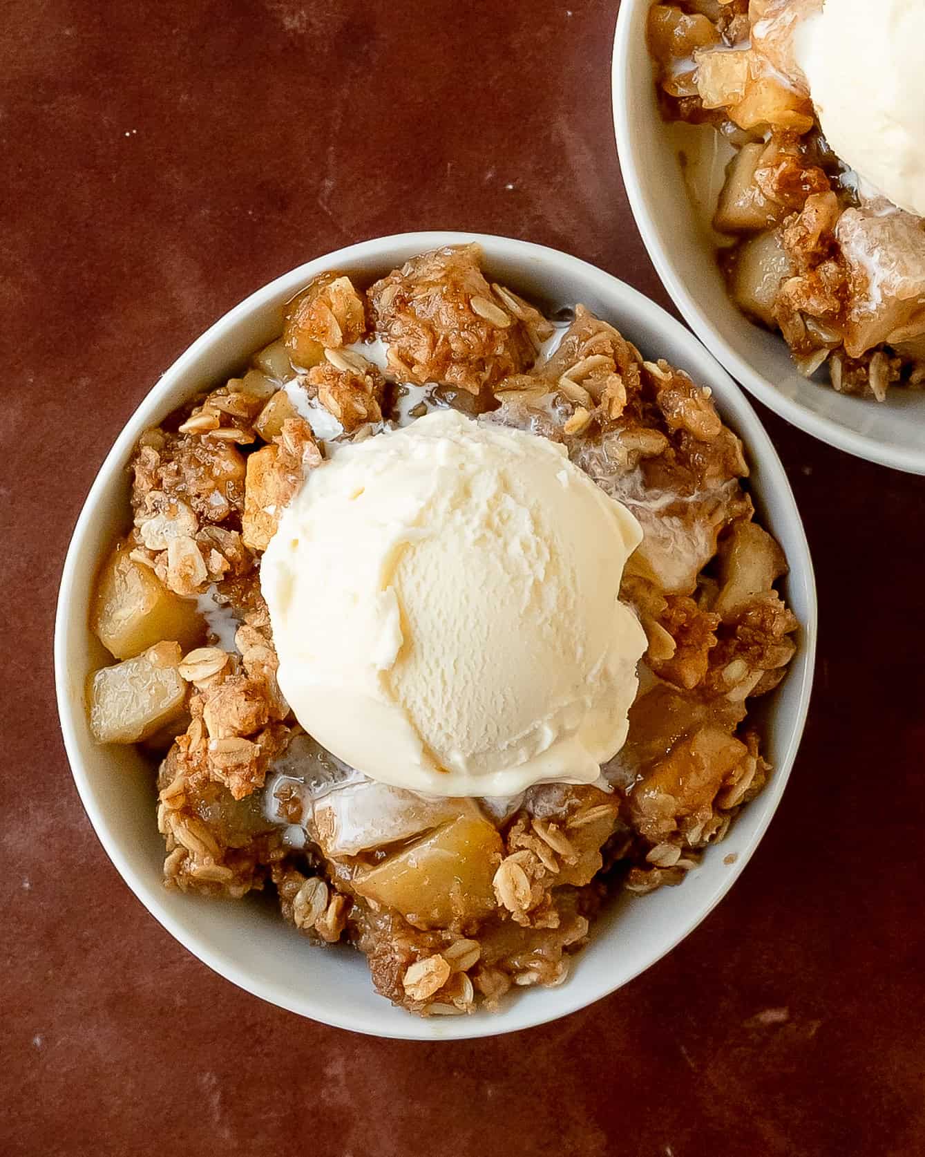 Warm cinnamon spiced pear crisp with golden oat crumble topping and vanilla ice cream in a bowl.