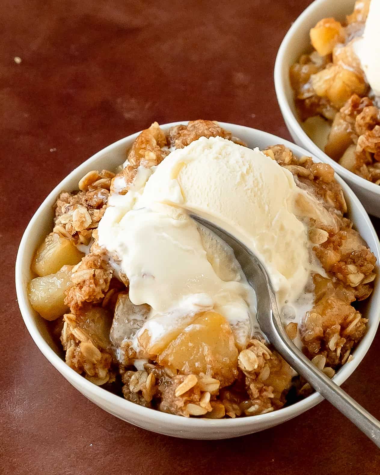 Individual serving of warm pear crisp with buttery crumble and melting vanilla ice cream.