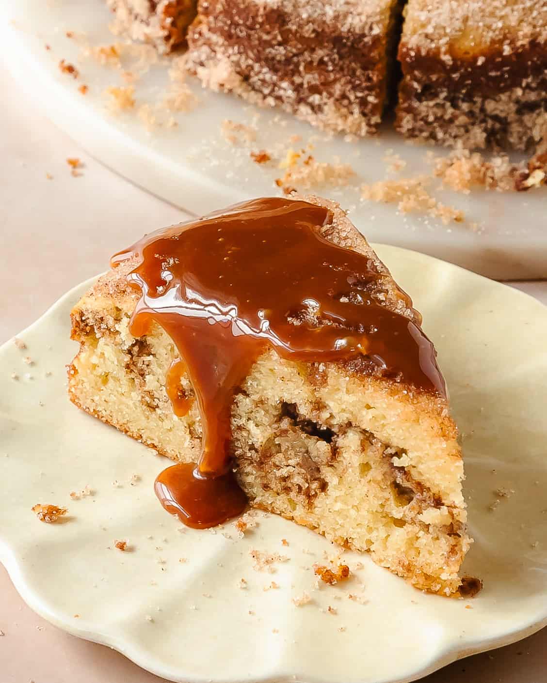 Slice of cinnamon cake showing the interior cinnamon swirl, the outside cinnamon sugar coating, all topped with a caramel drizzle.