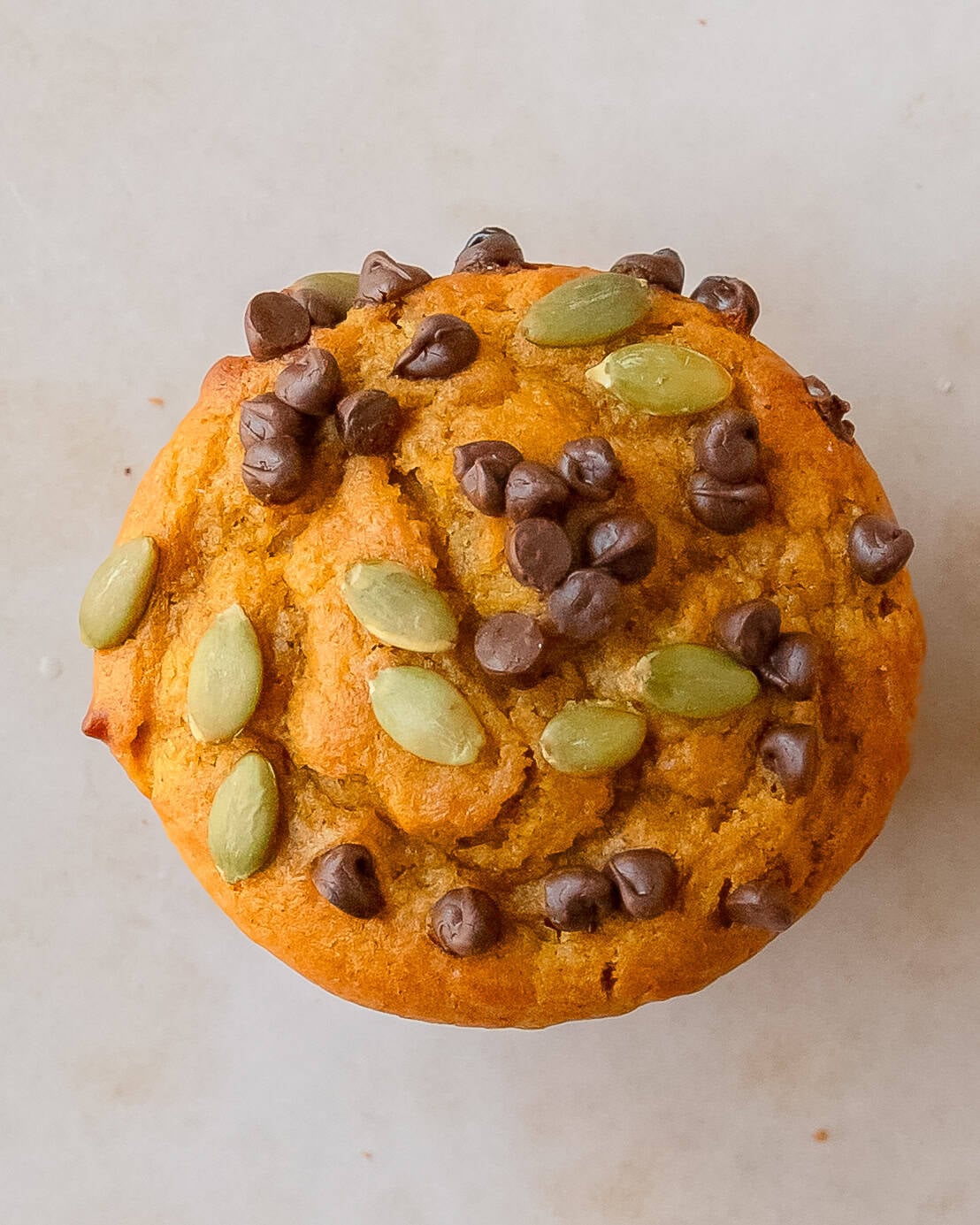 Up close photo showing the soft, dome of the pumplin cottage cheese muffins topped with crunchy pumpkin seeds and melty chocolate chips.