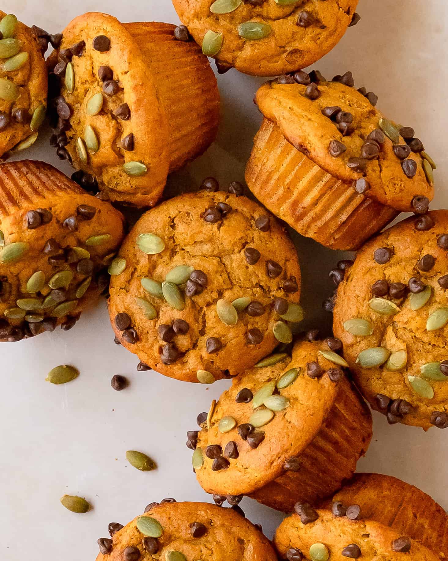Fluffy cottage cheese pumpkin muffins scattered to show the domed tops with chocolate chips and pumpkin seeds.