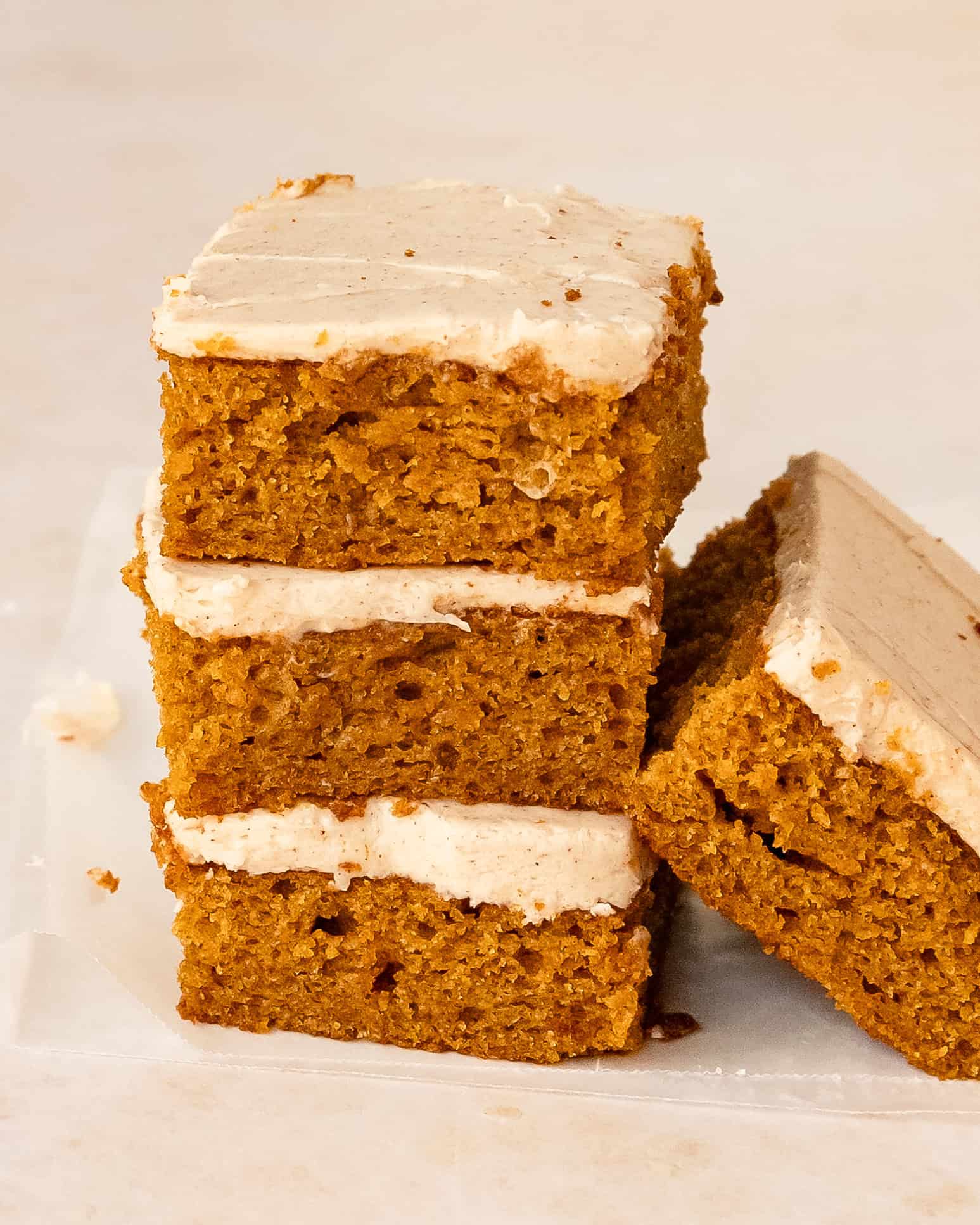 Soft pumpkin bars with a thick layer of cinnamon cream cheese frosting stacked to show the fluffy pumpkin cake layer and creak cheese frosting.