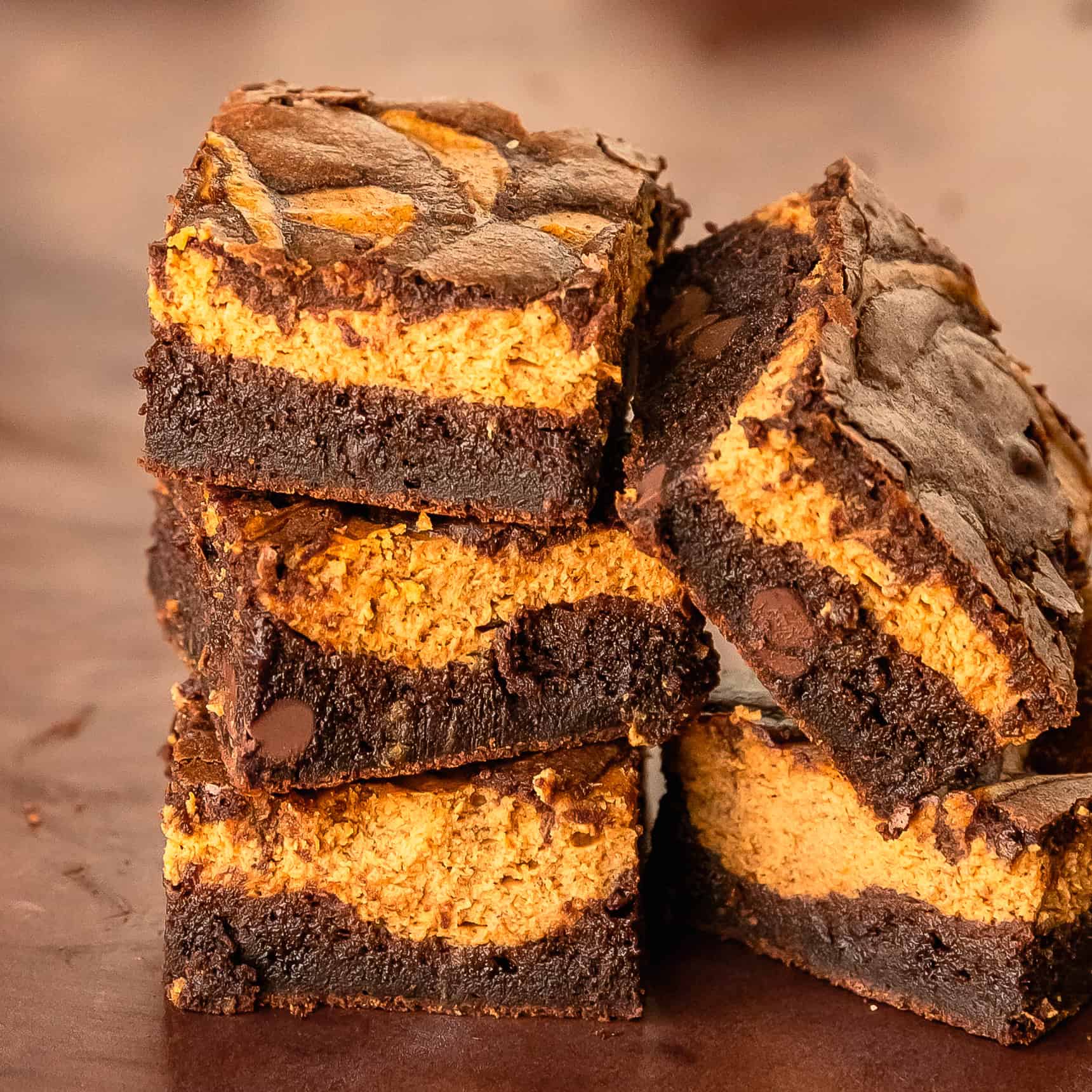 A stack of rich, fudgy pumpkin brownies showing their soft chocolate centers and slightly crinkled tops. Cozy natural lighting, warm autumn tones, and an inviting homemade feel make these brownies look irresistible.