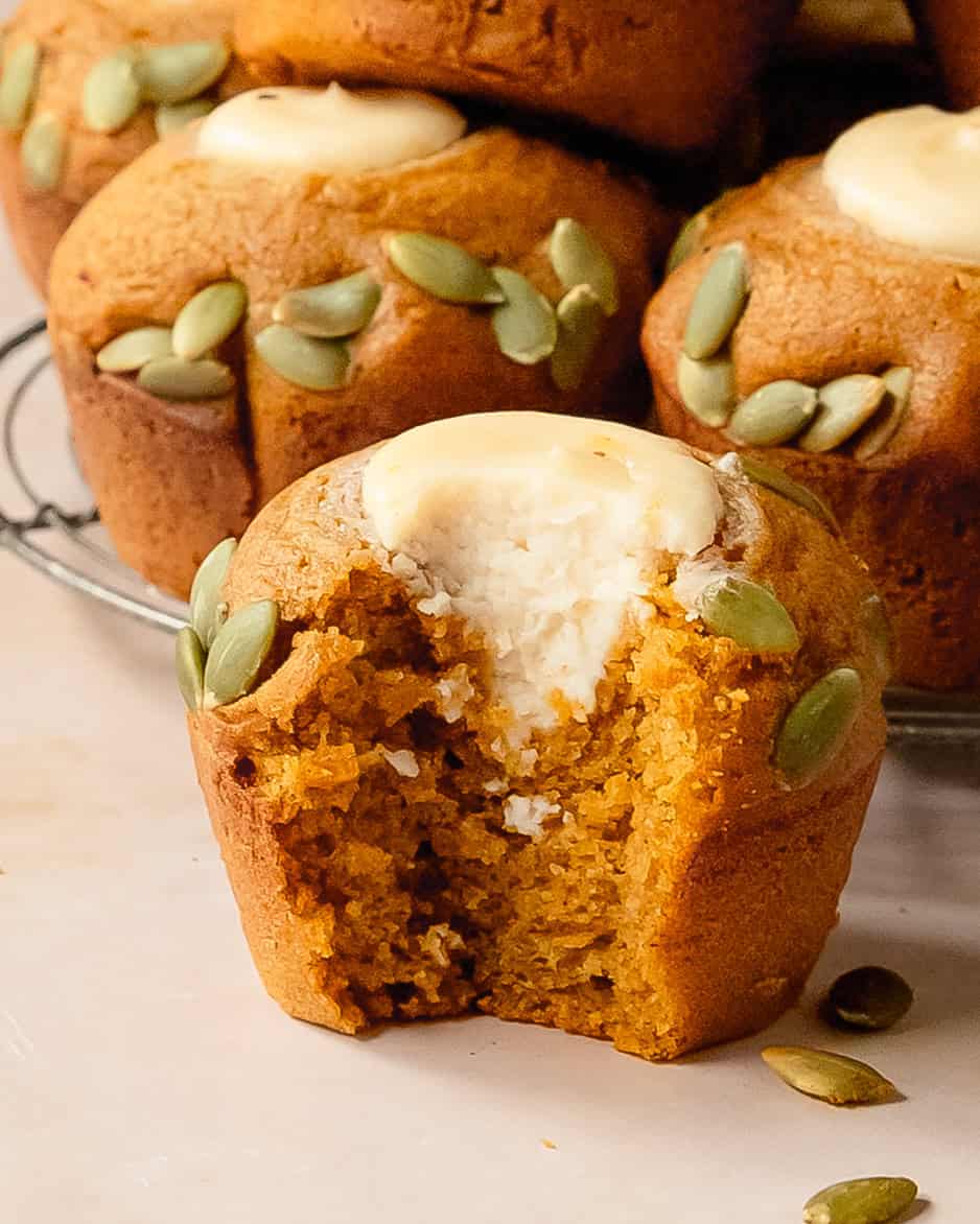 Close-up of a bite into a soft pumpkin muffin with cream cheese filling and pumpkin seed topping.
