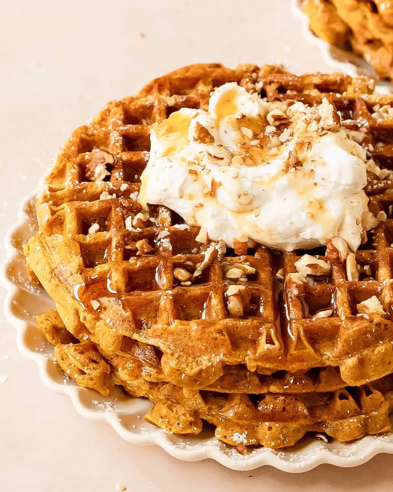 Stack of homemade pumpkin waffles topped with whipped cream and maple syrup.