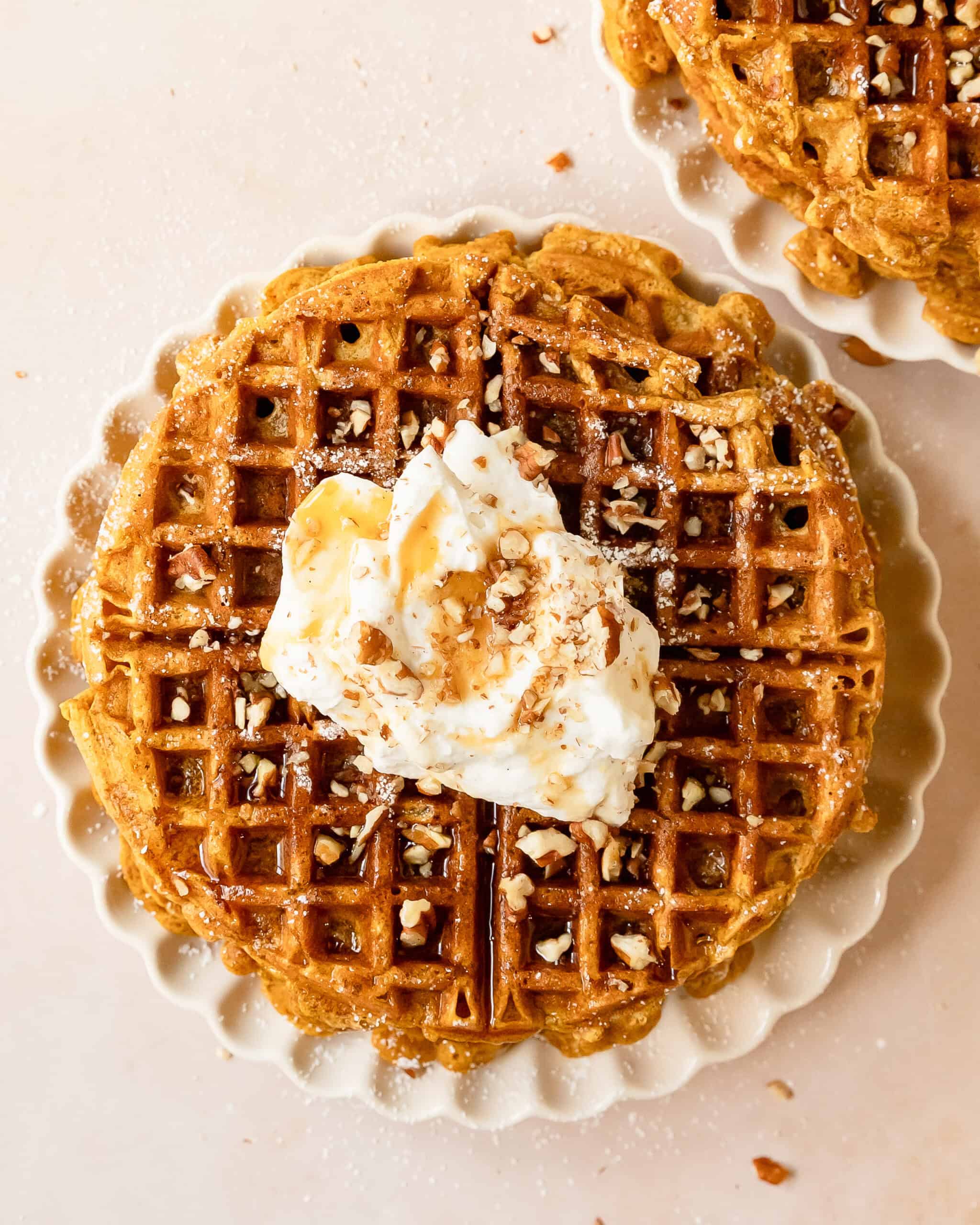 Close-up of fluffy pumpkin waffles with crisp golden edges topped with whipped cream, chopped nuts and maple syrup.