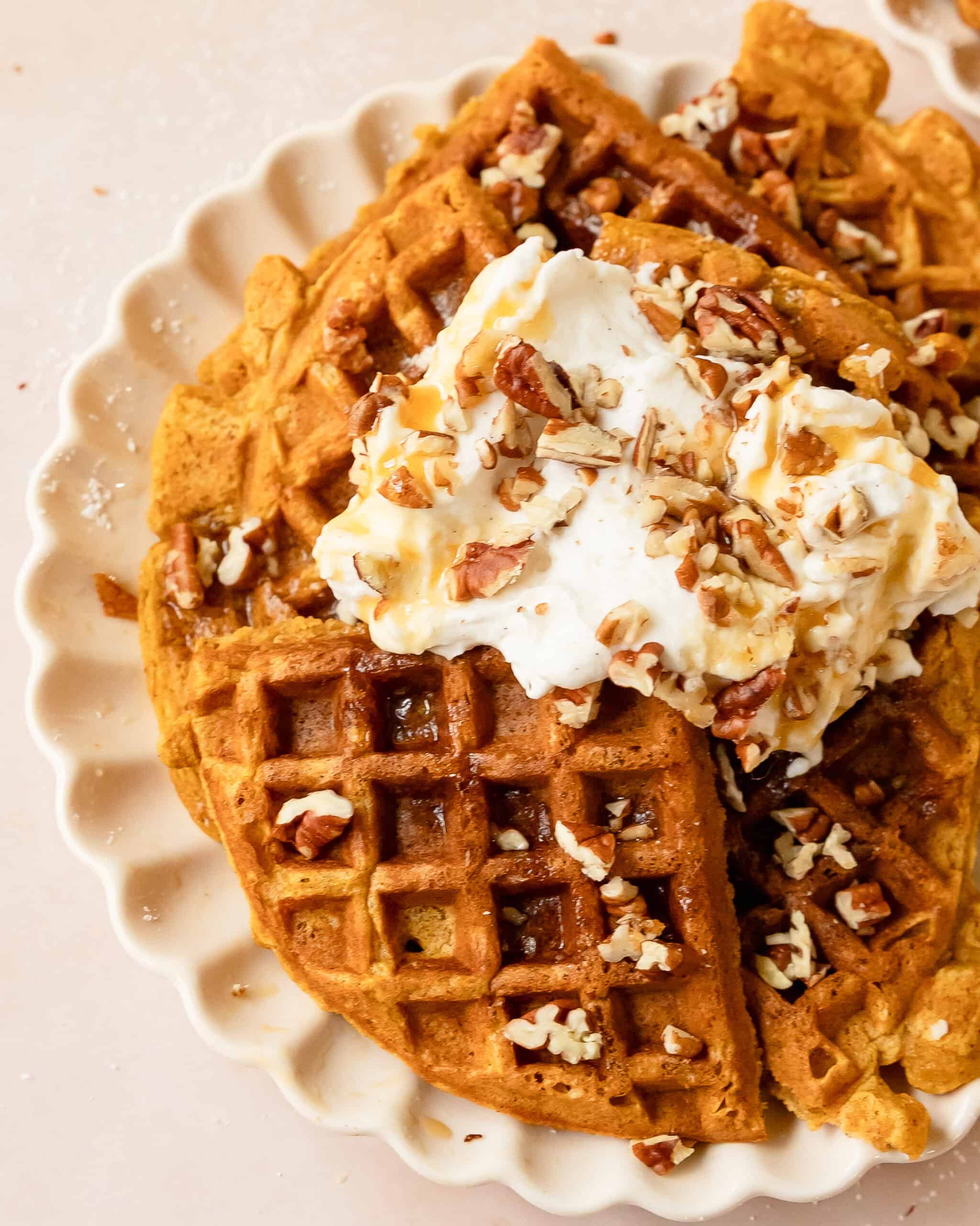 Close up photo of pumpkin waffle pieces topped with fluffy whipped cream and nuts.