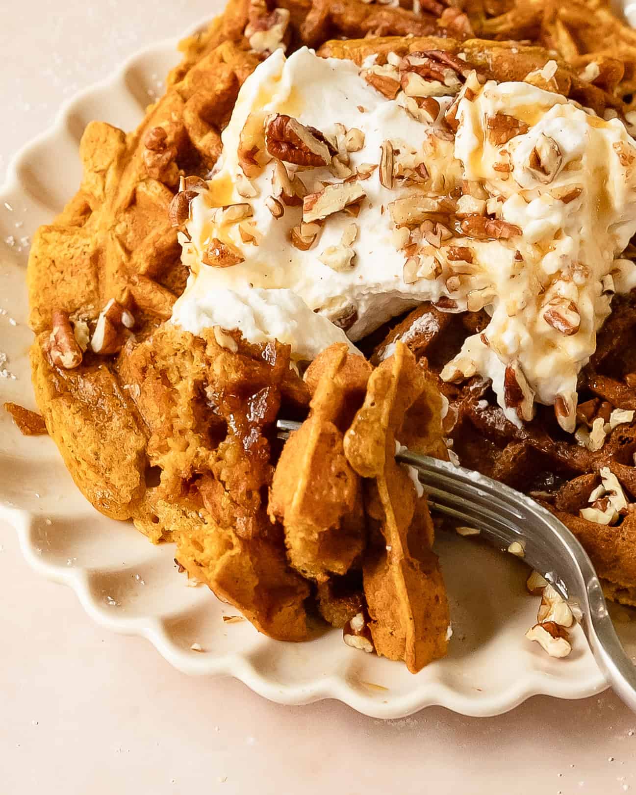 Stack of fluffy pumpkin waffles with some cut and on a fork to be eaten.
