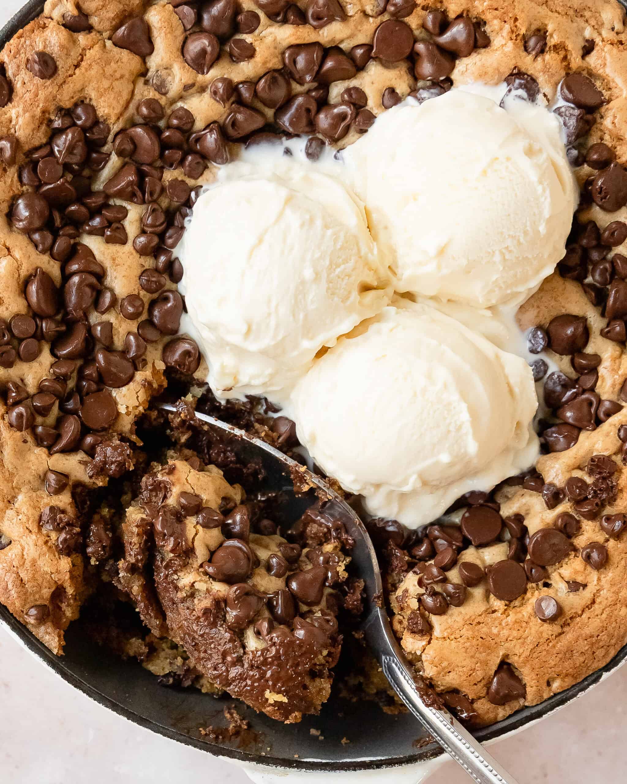 Easy chocolate chip skillet cookie with golden edges and a gooey center, topped with vanilla ice cream.
