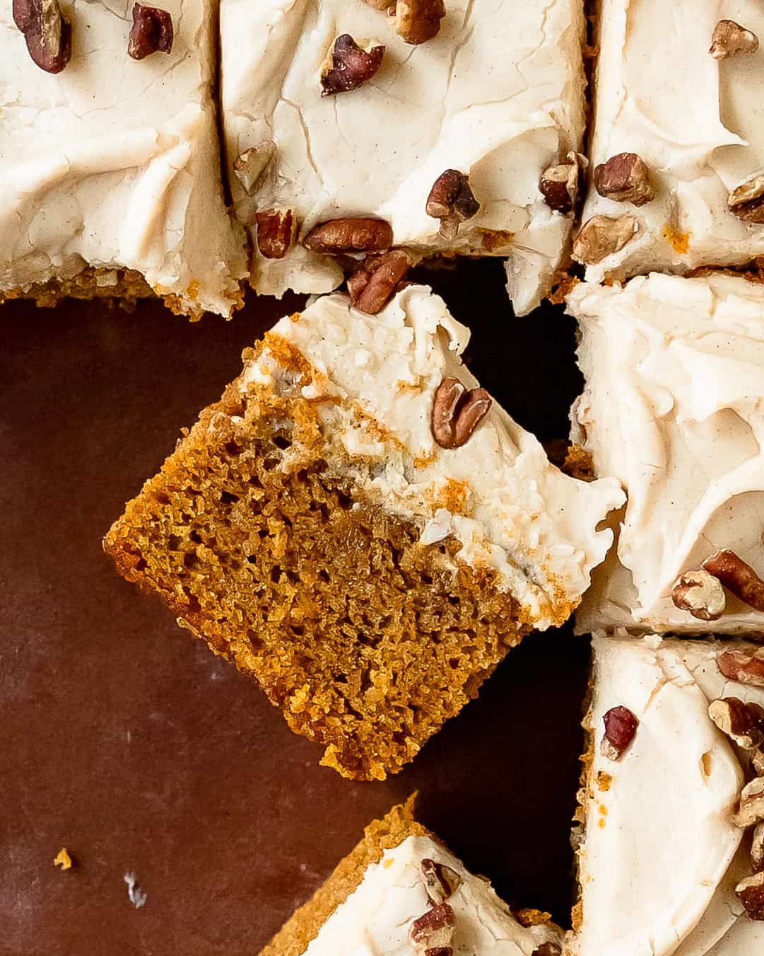 A slice of sweet potato cake showing its soft, tender orange interior topped with cream cheese frosting.